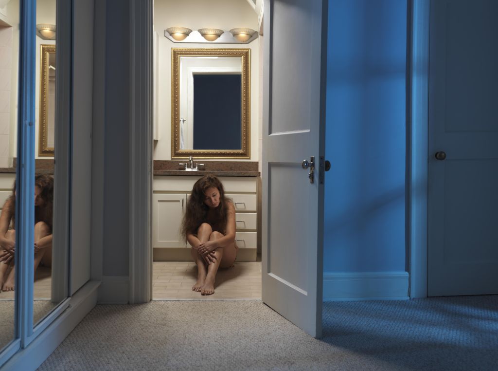 Woman sitting alone on a bathroom floor at night