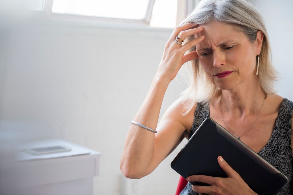 Frustrated Caucasian woman holding digital tablet suffering headache