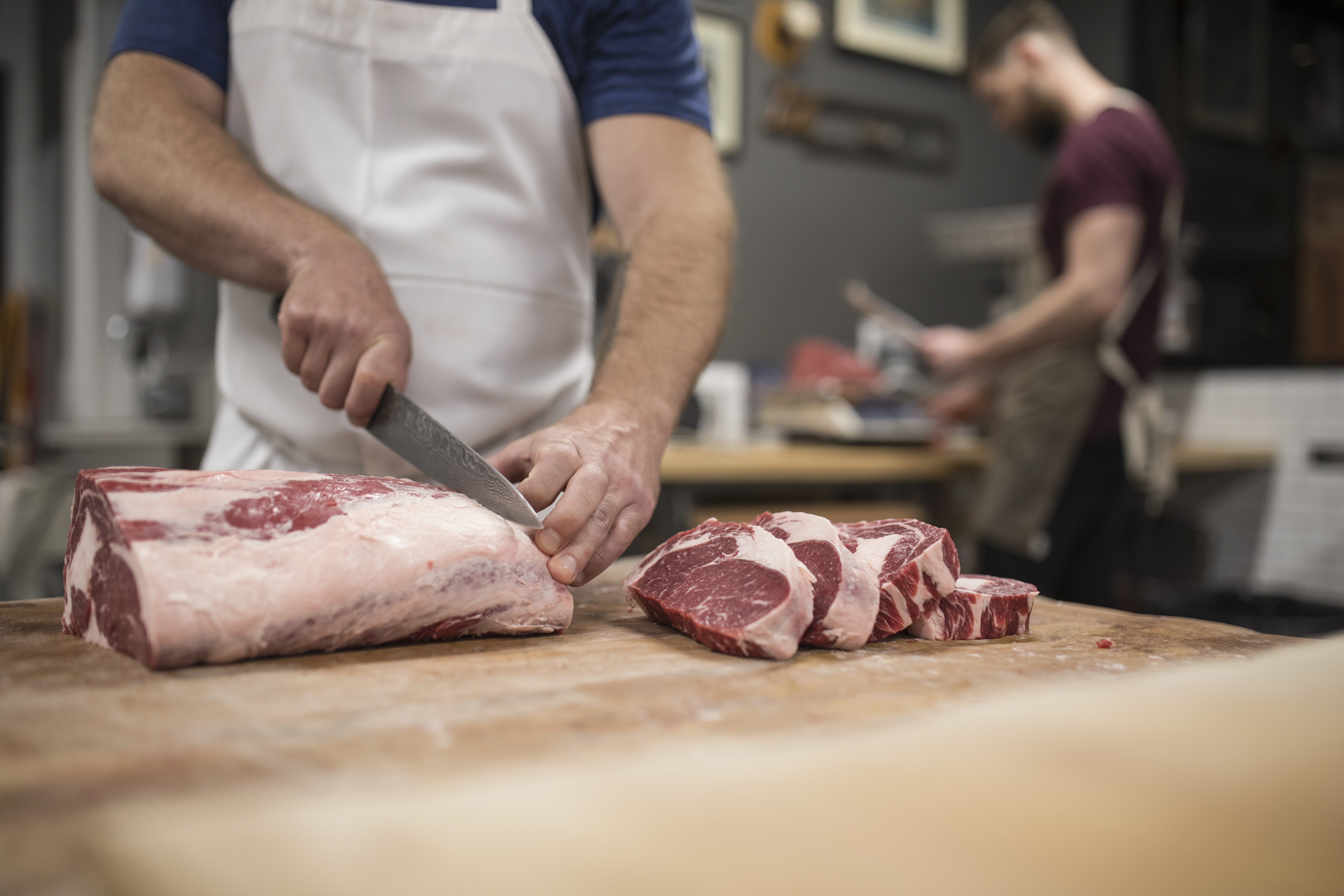 Male butcher with knife cutting into raw red meat in butcher