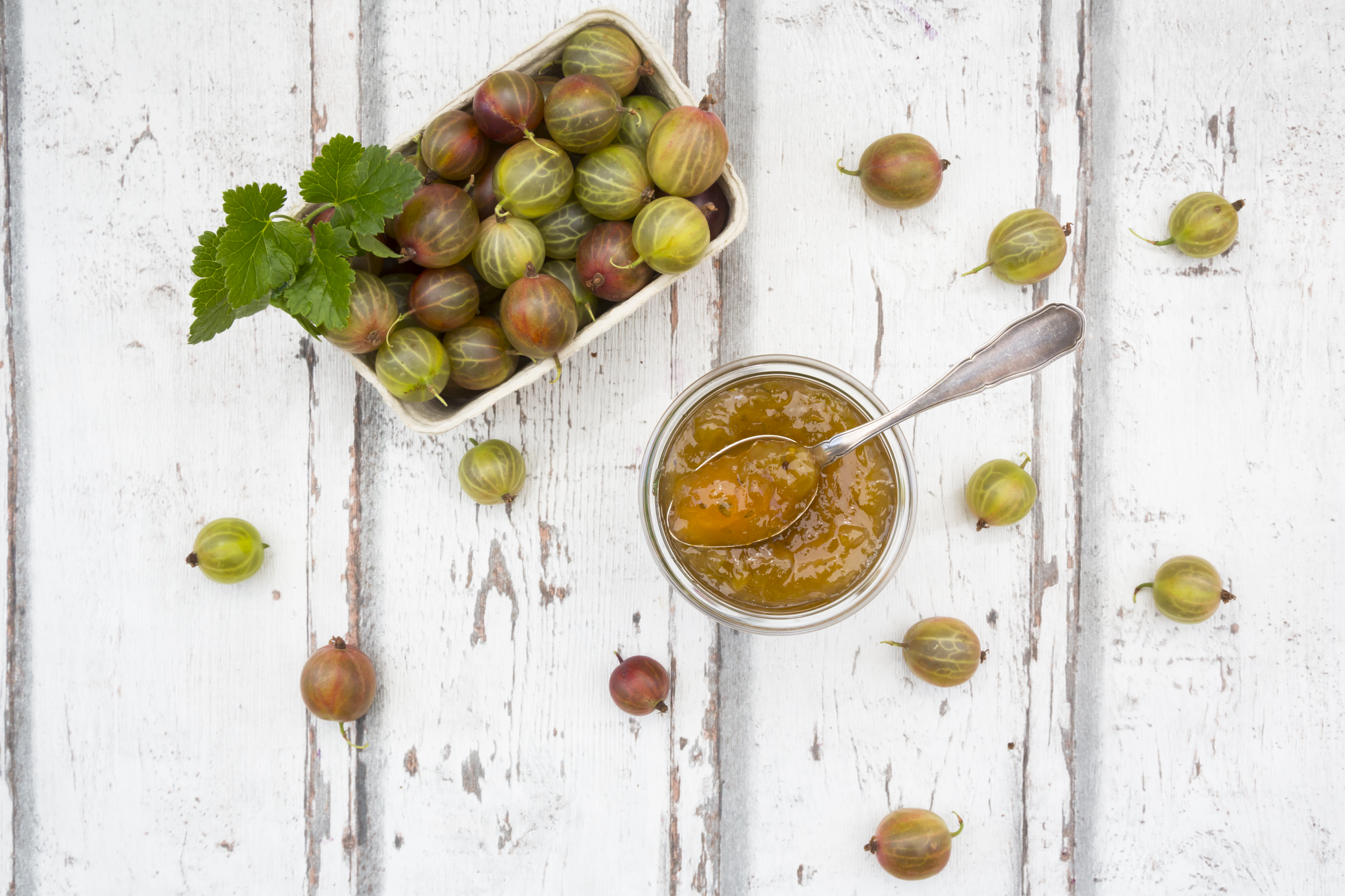 Cardboard box of gooseberries and jar of gooseberry jam on wood
