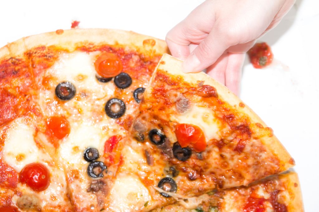 Cropped Image Of Hand Holding Pizza On Table