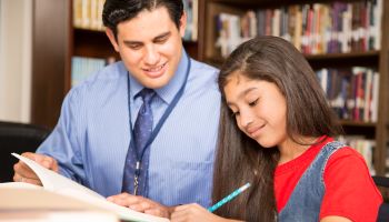 Teacher, mentor helps elementary-age schoolgirl with homework.