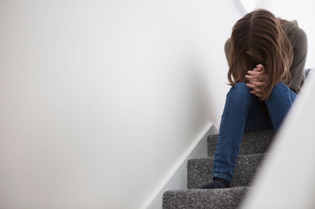 Teenage girl sitting on stairs with head down in despair