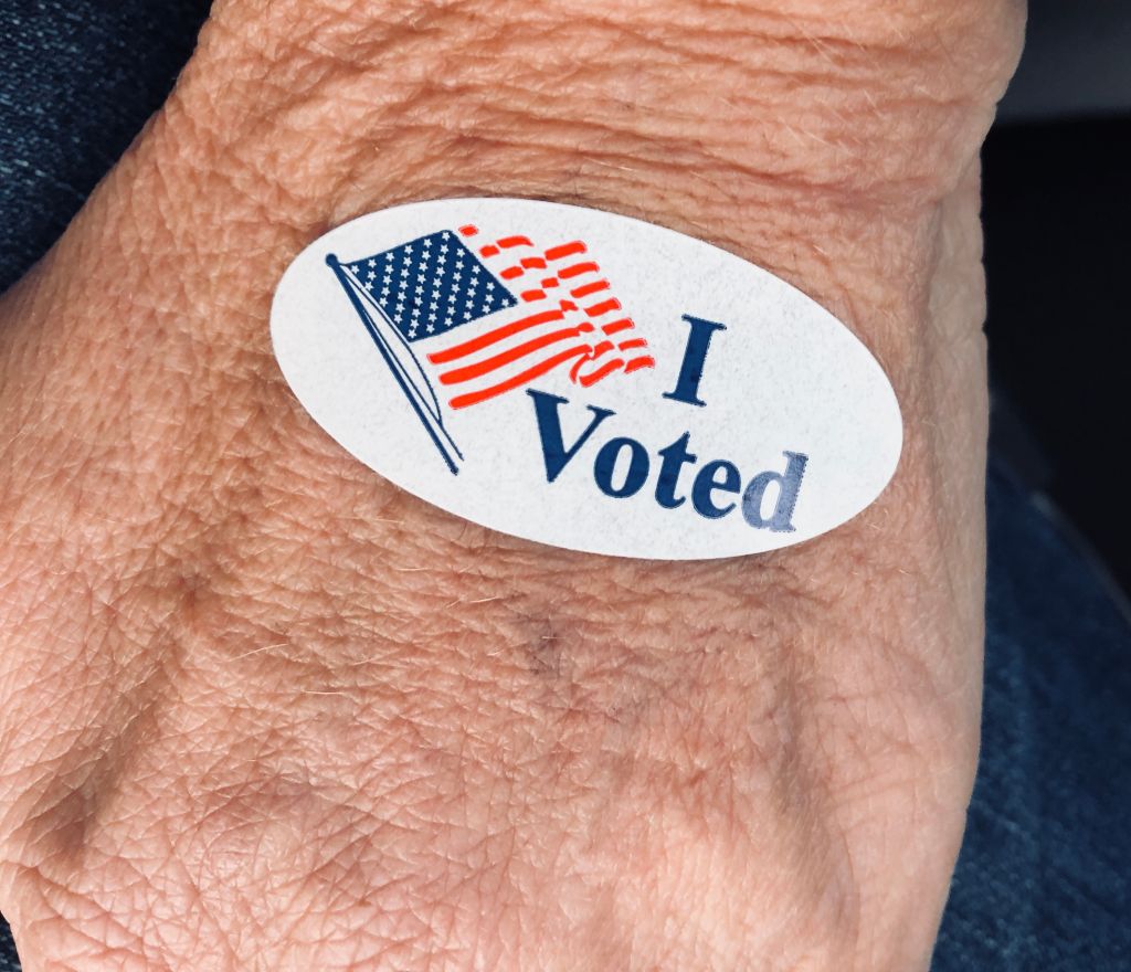 Senior woman’s hand displaying “I voted” sticker after early voting