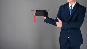 Midsection Of Businessman Holding Mortarboard Against Gray Background