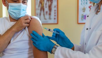 Female mature doctor or nurse giving shot or vaccine to a patient's shoulder. Vaccination and prevention against flu or virus pandemic.