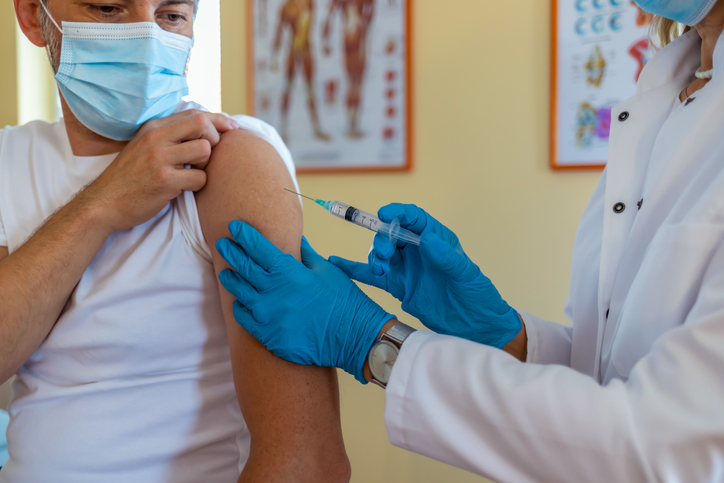 Female mature doctor or nurse giving shot or vaccine to a patient's shoulder. Vaccination and prevention against flu or virus pandemic.