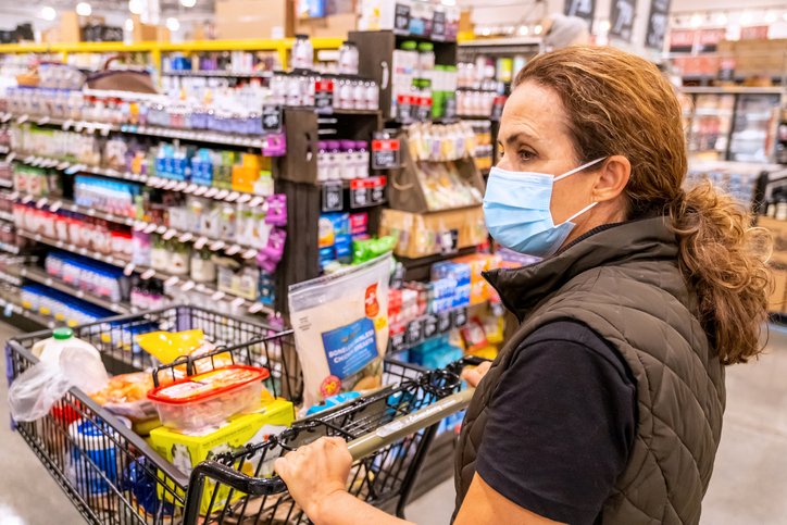 Mature woman wearing a protective face mask pushing a shopping cart while doing her grocery shopping at a local supermarket
