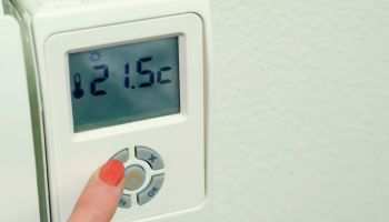 Close up of a woman's hand pushing a button of a digital thermostat on the radiator at home