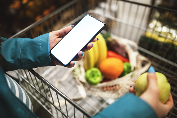 Shopping in vegetable aisle and using phone.