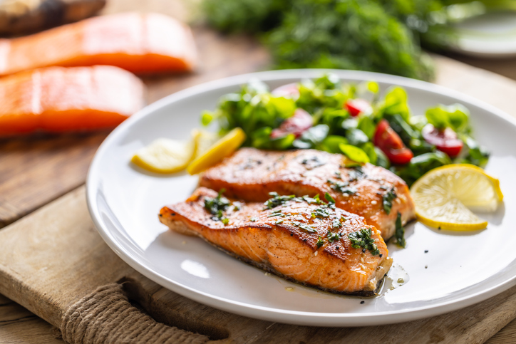 Two salmon fillets baked until crispy with parsley herbs, as a side salad marinated with tomatoes.