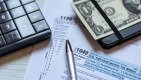 U.S. individual and corporation income tax return close-up next to a calculator, dollars, money, a pen and a notepad on a wooden table.