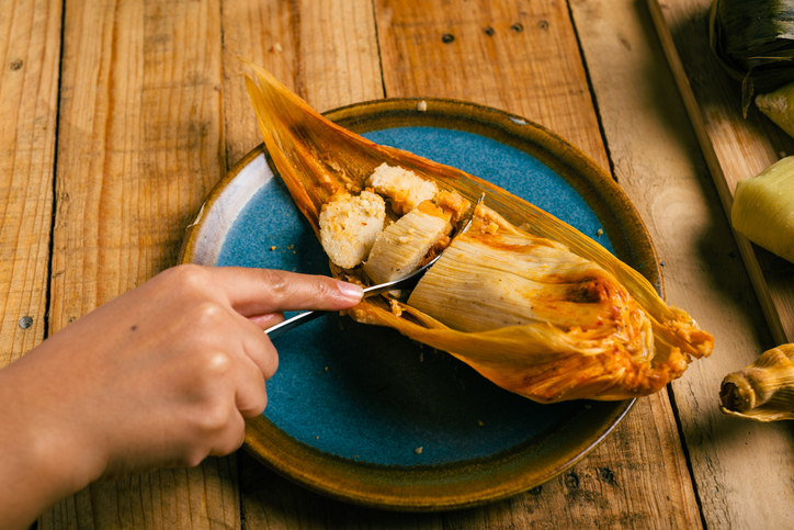 Hands of a person cutting a tamale with a fork. Tamale, typical Mexican food.
