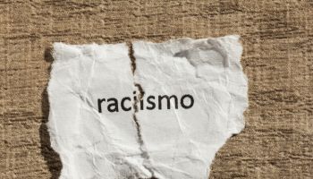Torn paper written racismo, portuguese and spanish word for racism, over wood table. Concept of old and abandoned idea or practice.