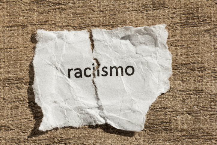 Torn paper written racismo, portuguese and spanish word for racism, over wood table. Concept of old and abandoned idea or practice.