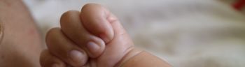 one hand of a newborn in a grasping position with the thumb inside