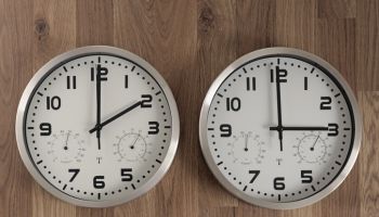 Two clocks, one showing two o'clock, the other showing three o'clock. Time change symbol.