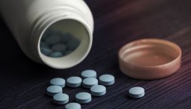 Medication bottle and blue pills spilled over blue wood background. Pharmaceutical drugs.