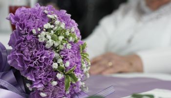 Closeup shot of a purple bridal bouquet with the elder bride in the background