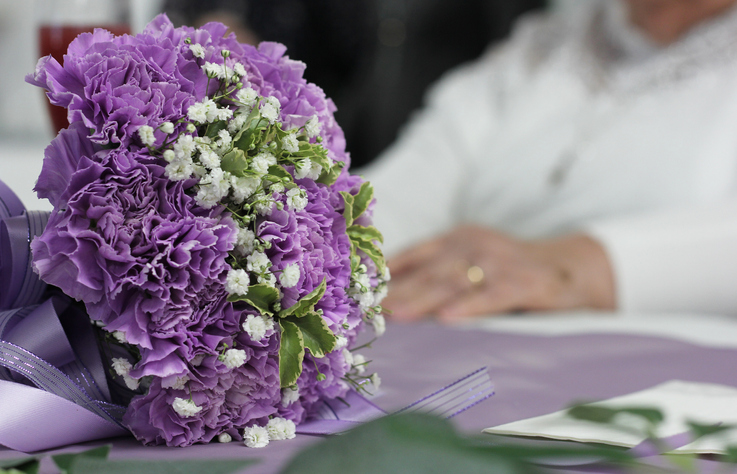 Closeup shot of a purple bridal bouquet with the elder bride in the background