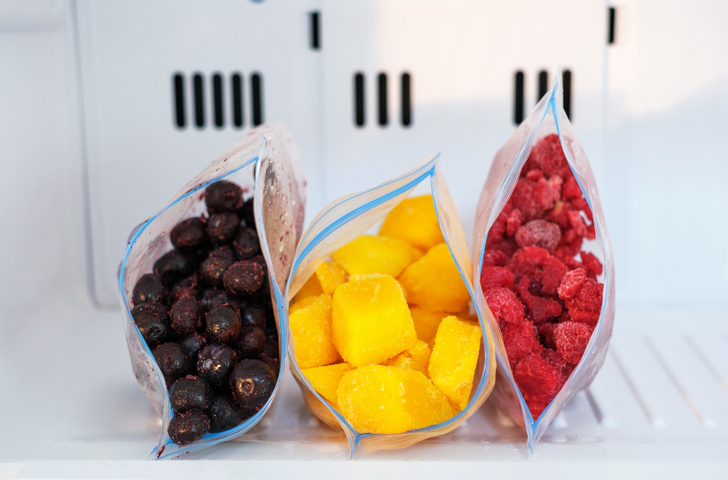 Frozen fruits and berries in plastic bags in freezer close-up.