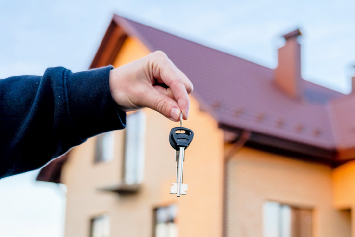 Hand holding key in front of home. Real estate, leasing insurance and purchase concept