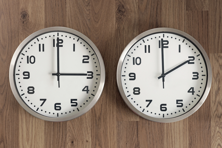 Two clocks, one showing three o'clock, the other showing two o'clock. Time change symbol.