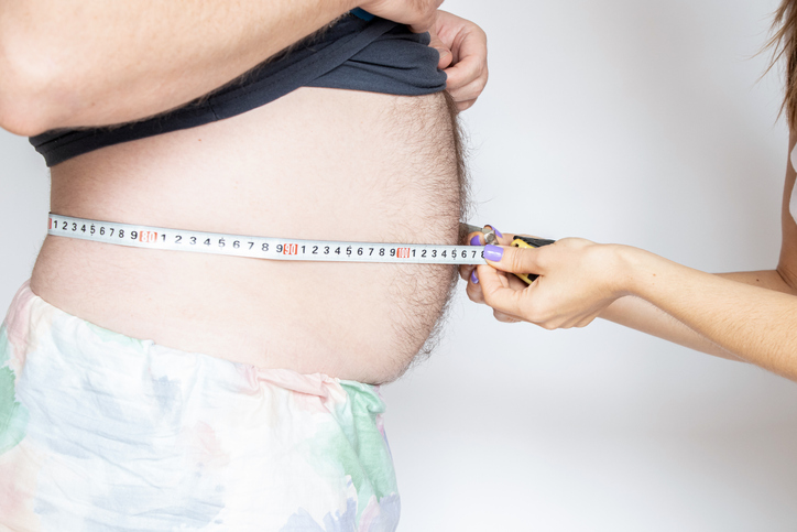 A woman measures an overweight man's belly with a measuring tape on a light background, obesity and diet
