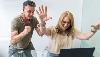 Cheerful husband and wife shopped from home using notebook and credit card while raising arms up