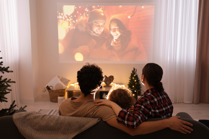 Family watching Christmas movie via video projector at home, back view
