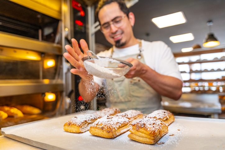 Worker pouring powdered sugar on delicious pastries on a bakery