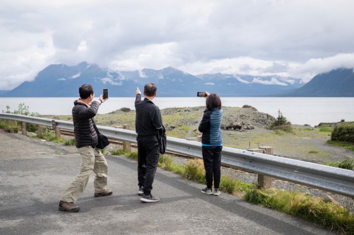 Tourists having fun and taking photos of mountains using smartphones. Seward waterfront. Alaska.