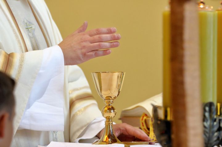Chalice on the altar and priest celebrating mass in the background