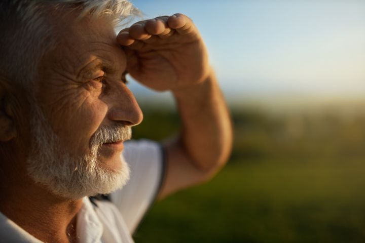 Bearded man squinting from bright sun, while looking into distance during trip.