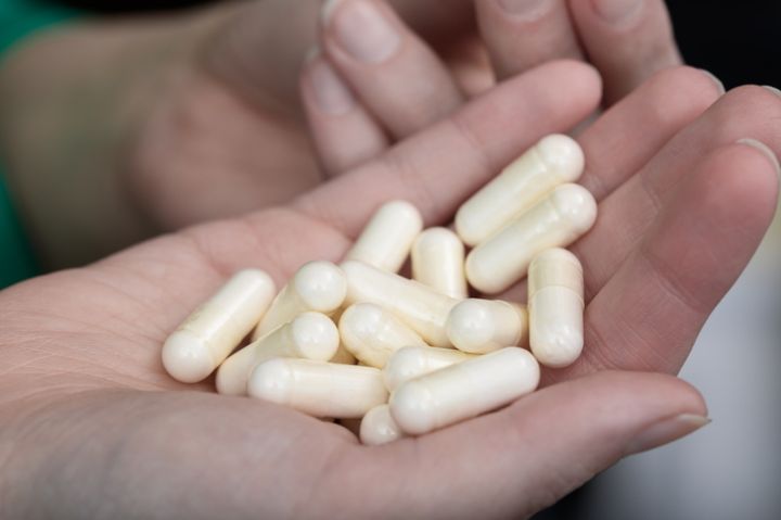 Transparent capsules, dietary supplements, held in a woman's hand, light powder inside