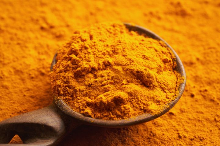 Ground turmeric root powder on a wooden spoon