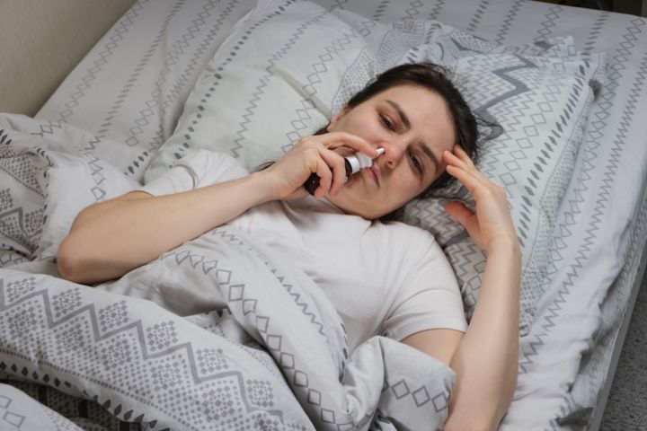 A woman with rhinitis squeaks a saline solution or vasoconstrictor drops into the nose lying in bed, top view.