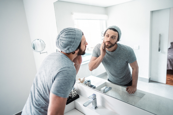 Mid adult man checking his beard in the bathroom's mirror