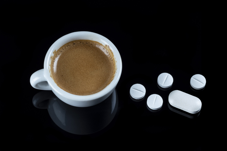 Cup of espresso coffee and five medicine pills on black background.