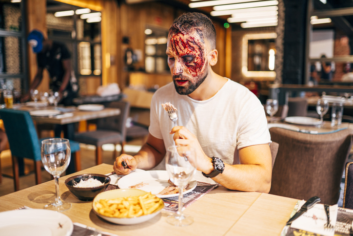 Man with makeup on his face with wounds and blood. Eating at the table