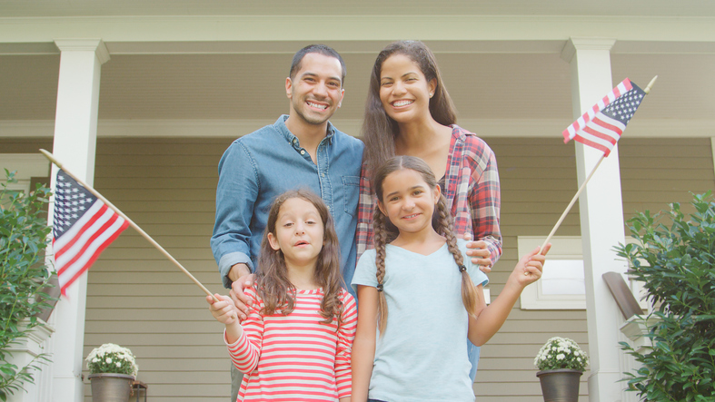 Portrait Of Family Outside House Holding American Flags