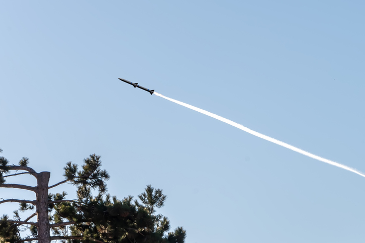The rocket takes off into the sky, leaving behind a trail against the blue sky and forest,