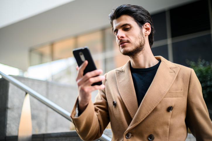 Young businessman reading a message on his smartphone while walking down the stairs