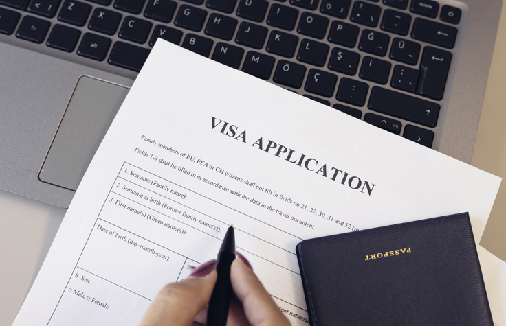 Woman filling form for immigration. Visa application form, hand holding pen, computer and passport on desk.