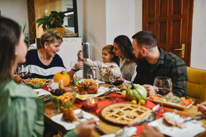 Little Nephew Giving Piece of Meat To Grandmother While Sitting on Mother's Lap on Dinner