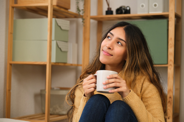 Young woman relaxing at home, drinking coffee and daydreaming