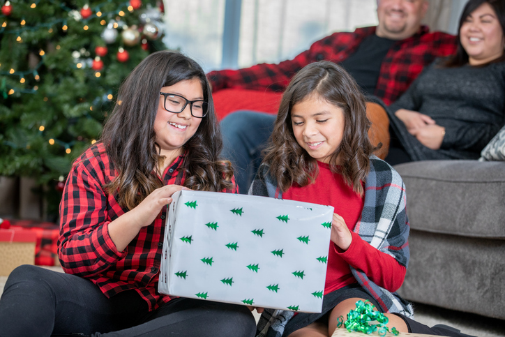 Two young siblings opening Christmas presents in living room with family
