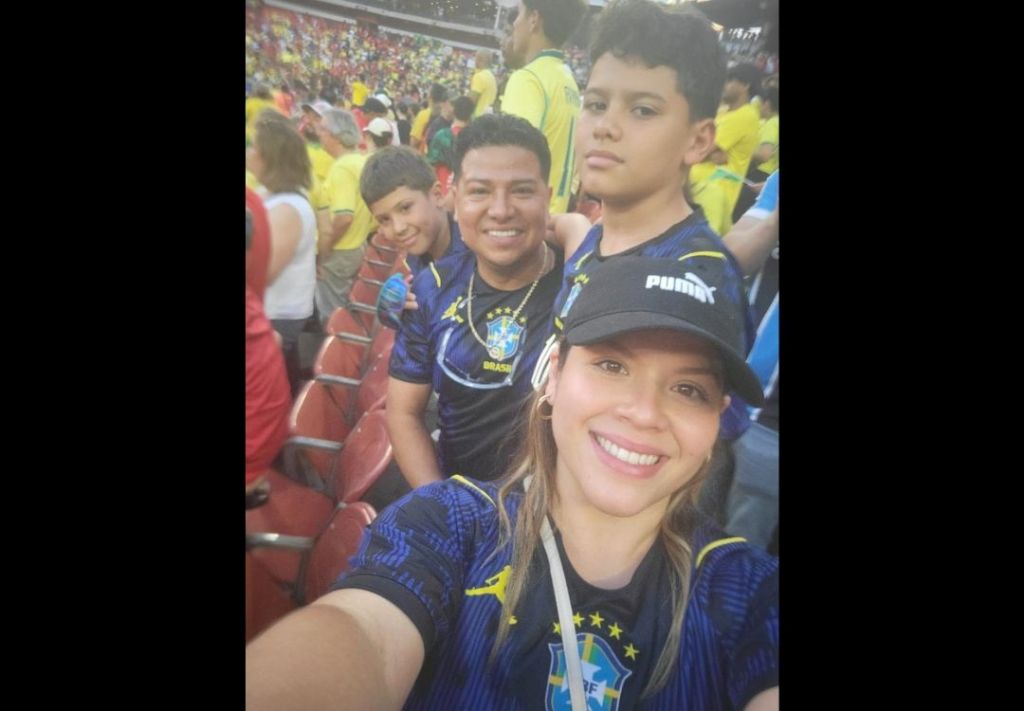A group of people wearing Puma jerseys and hats, smiling and posing for a selfie at a crowded stadium.