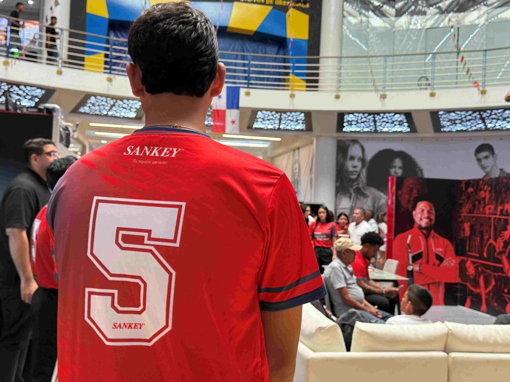 A person wearing a red jersey with the text "SANKEY 5" on the back, standing in a crowded indoor space with various displays and signage visible.