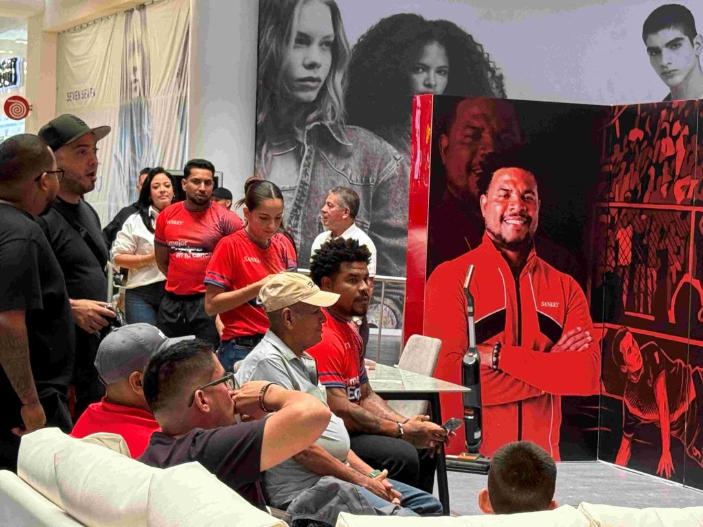 A group of people wearing red shirts gathered around a large poster featuring portraits of people, likely a promotional event or gathering.